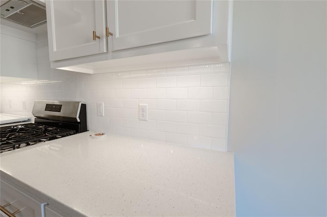 kitchen featuring white cabinetry, stainless steel gas stove, light stone counters, backsplash, and exhaust hood