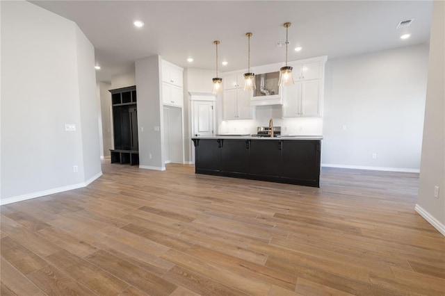 kitchen with sink, decorative light fixtures, light hardwood / wood-style flooring, white cabinetry, and an island with sink