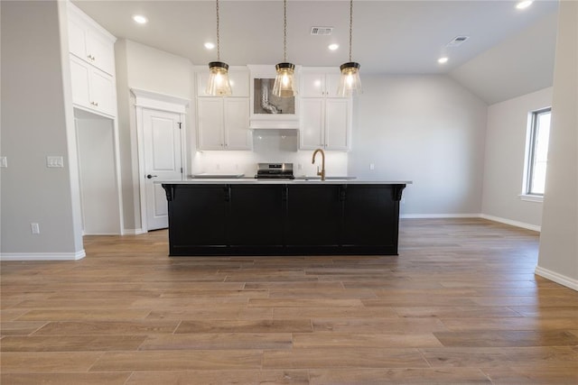 kitchen featuring a kitchen island with sink, white cabinets, sink, hanging light fixtures, and light hardwood / wood-style floors