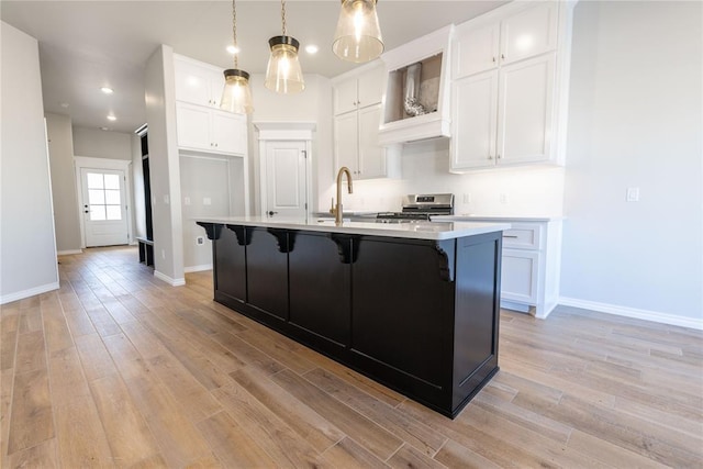 kitchen featuring light wood-type flooring, decorative light fixtures, stainless steel range oven, white cabinetry, and an island with sink