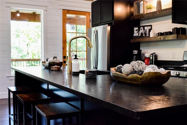 kitchen with stainless steel fridge, dark wood-type flooring, wood walls, and range