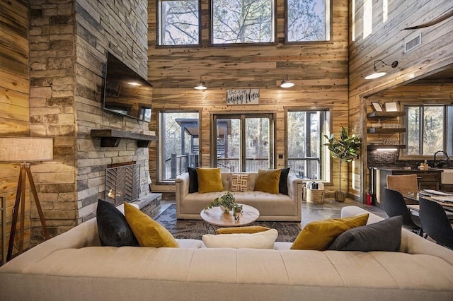 living room featuring plenty of natural light, wood walls, a stone fireplace, and a high ceiling