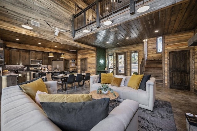 living room with wood walls, a towering ceiling, concrete flooring, and wooden ceiling