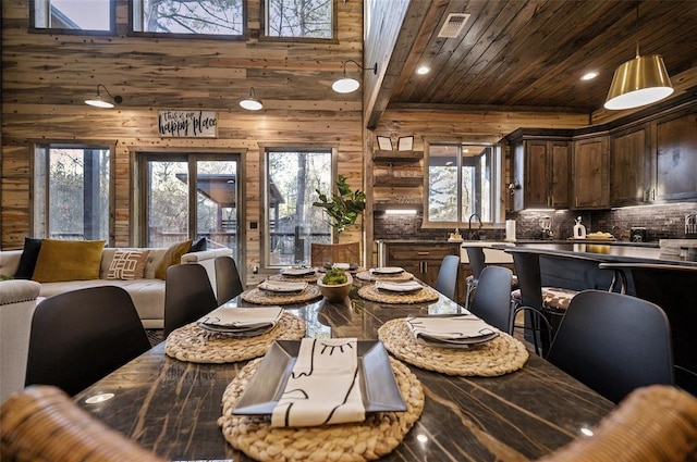 dining area with beam ceiling, sink, a high ceiling, wooden walls, and wood ceiling