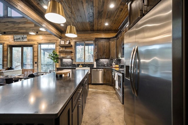 kitchen featuring wooden walls, appliances with stainless steel finishes, decorative light fixtures, a kitchen island, and dark brown cabinets