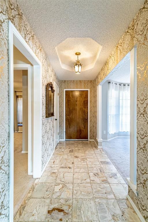 hall with a raised ceiling, a textured ceiling, and a notable chandelier