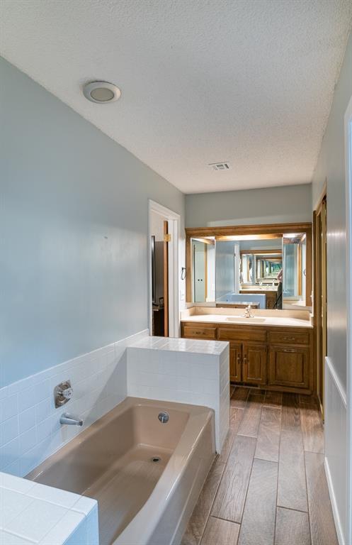 bathroom featuring a bath, wood-type flooring, a textured ceiling, and sink