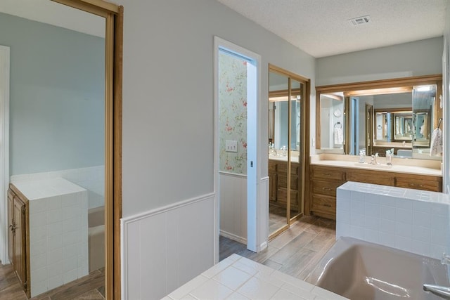 bathroom with vanity, a tub to relax in, a textured ceiling, and hardwood / wood-style flooring