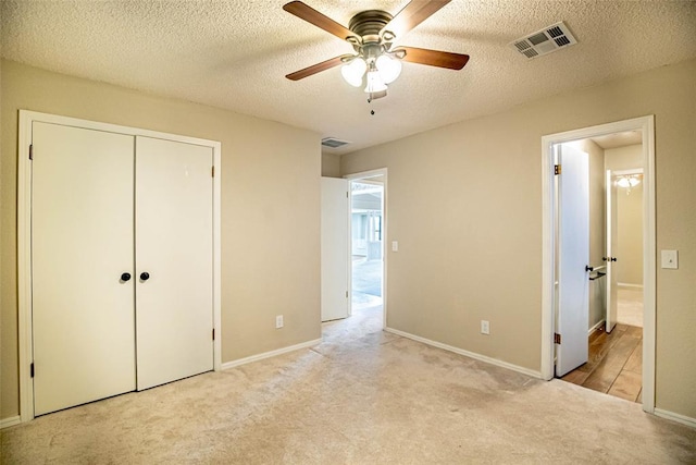 unfurnished bedroom with a textured ceiling, ceiling fan, light carpet, and a closet