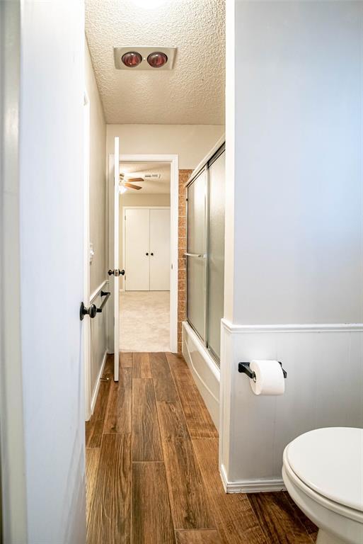 bathroom featuring combined bath / shower with glass door, hardwood / wood-style floors, a textured ceiling, and toilet