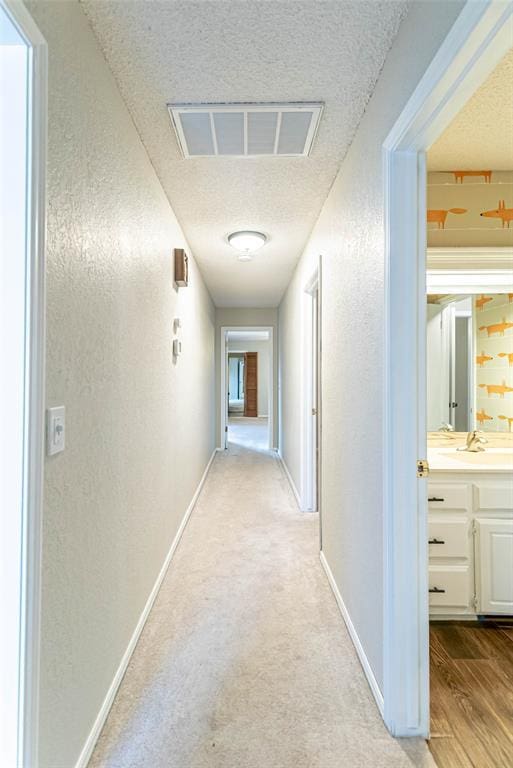 corridor featuring a textured ceiling and light colored carpet