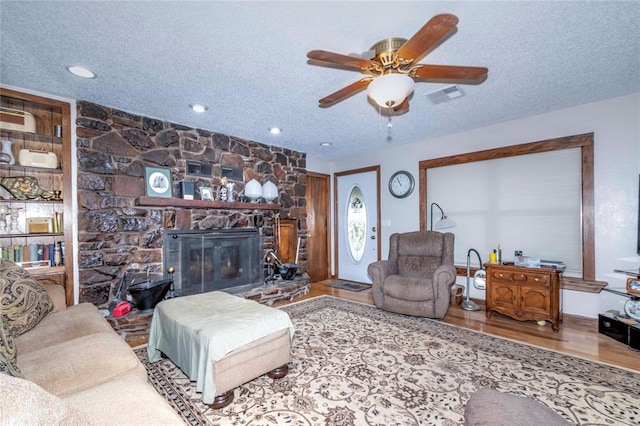 living room featuring a fireplace, ceiling fan, wood-type flooring, and a textured ceiling