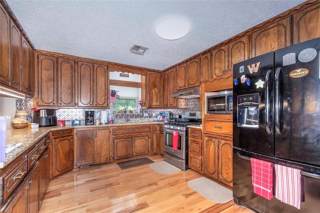 kitchen featuring light wood-type flooring, a textured ceiling, appliances with stainless steel finishes, and tasteful backsplash