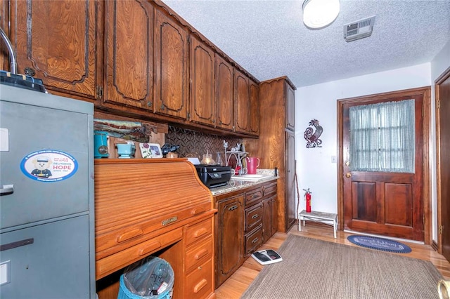 kitchen with decorative backsplash, sink, light wood-type flooring, and a textured ceiling