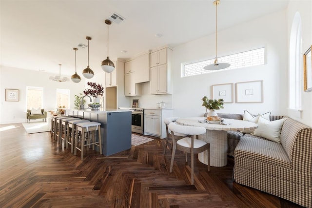 kitchen featuring dark parquet flooring, stainless steel range, pendant lighting, a breakfast bar, and a kitchen island