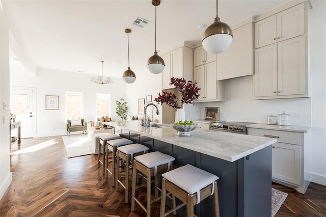 kitchen with a center island with sink, light stone counters, and hanging light fixtures