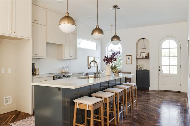 kitchen with dark parquet flooring, sink, an island with sink, and pendant lighting