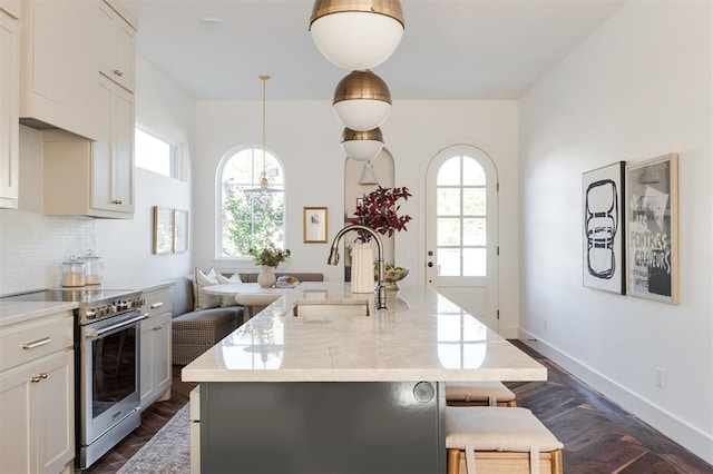 kitchen featuring decorative light fixtures, a healthy amount of sunlight, high end stainless steel range oven, and an island with sink