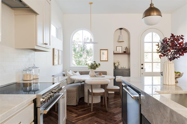 kitchen with a wealth of natural light, dark parquet flooring, hanging light fixtures, and stainless steel stove