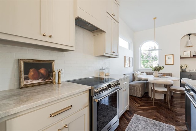 kitchen with dark parquet flooring, hanging light fixtures, high end stainless steel range, tasteful backsplash, and light stone counters