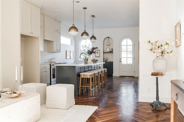 kitchen featuring pendant lighting, dark parquet floors, a center island with sink, and a healthy amount of sunlight