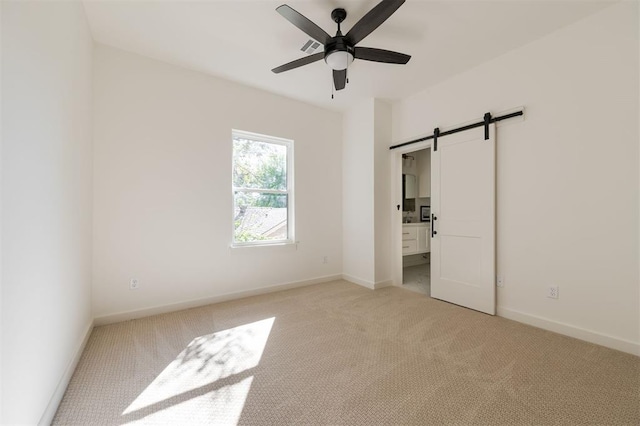 unfurnished bedroom with light carpet, connected bathroom, ceiling fan, and a barn door