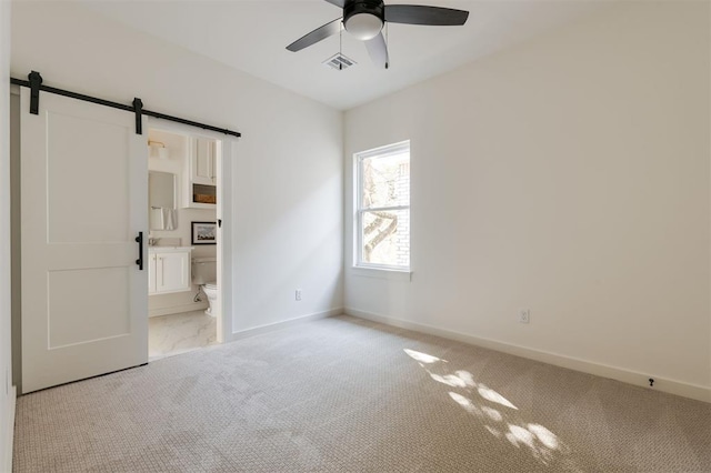 unfurnished bedroom featuring connected bathroom, ceiling fan, light carpet, and a barn door