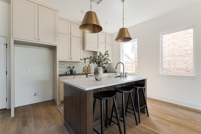 kitchen featuring pendant lighting, backsplash, sink, hardwood / wood-style flooring, and an island with sink