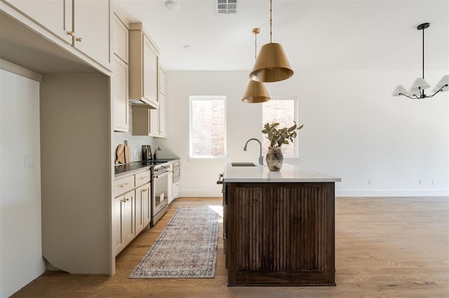 kitchen featuring light wood-type flooring, sink, stainless steel stove, hanging light fixtures, and an island with sink