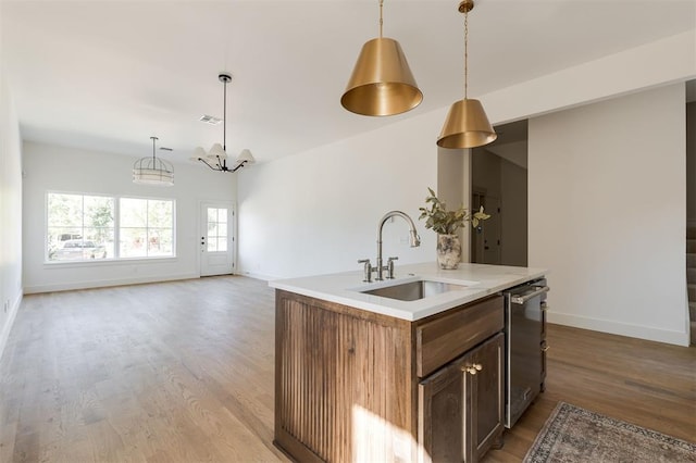 kitchen featuring dishwasher, a kitchen island with sink, hanging light fixtures, sink, and light hardwood / wood-style flooring