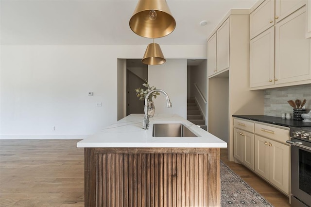 kitchen with cream cabinets, a center island with sink, sink, decorative backsplash, and decorative light fixtures