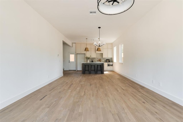 unfurnished living room with plenty of natural light, an inviting chandelier, and light wood-type flooring