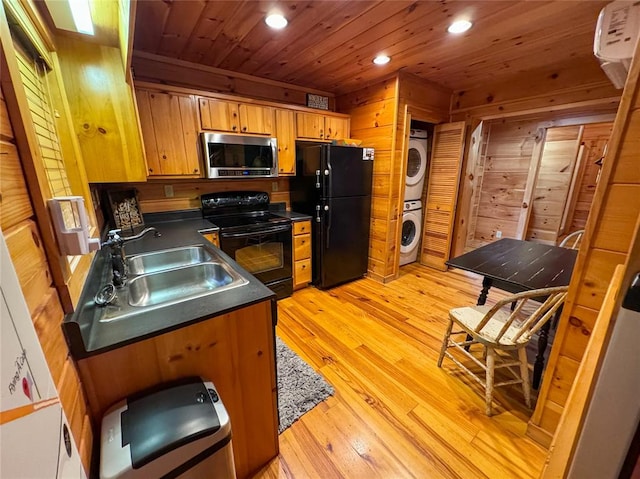 kitchen with wood walls, stacked washer and clothes dryer, black appliances, sink, and light hardwood / wood-style flooring