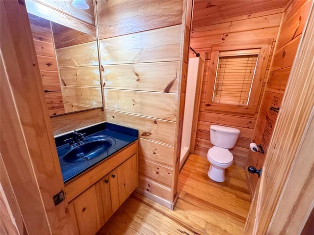 bathroom with hardwood / wood-style flooring, vanity, toilet, and wooden walls