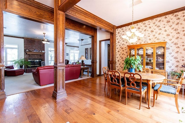 dining room with ceiling fan with notable chandelier, crown molding, a fireplace, wood-type flooring, and decorative columns