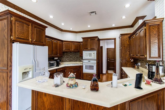 kitchen featuring backsplash, kitchen peninsula, crown molding, and white appliances