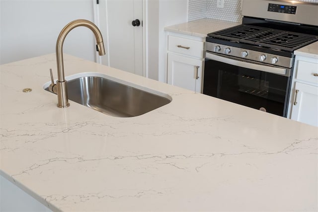 kitchen featuring white cabinets, stainless steel gas stove, light stone countertops, and sink