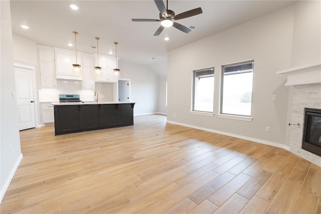 unfurnished living room featuring a stone fireplace, lofted ceiling, sink, ceiling fan, and light hardwood / wood-style floors