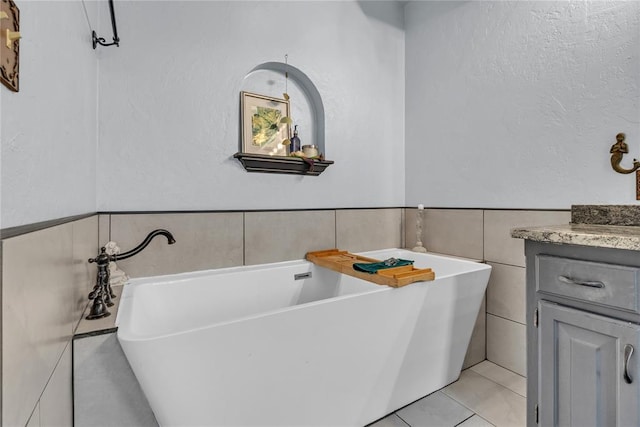 bathroom with tile patterned flooring, vanity, a tub to relax in, and tile walls