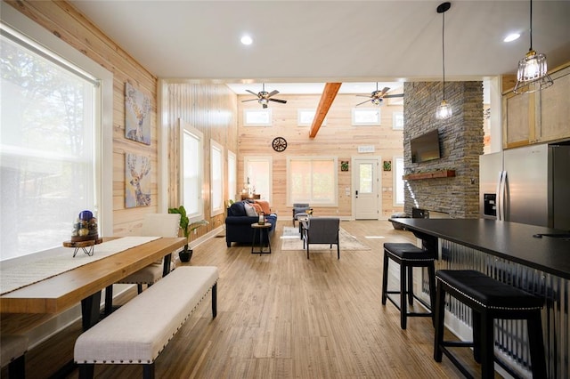 dining space featuring light wood-type flooring, ceiling fan, wooden walls, beam ceiling, and high vaulted ceiling