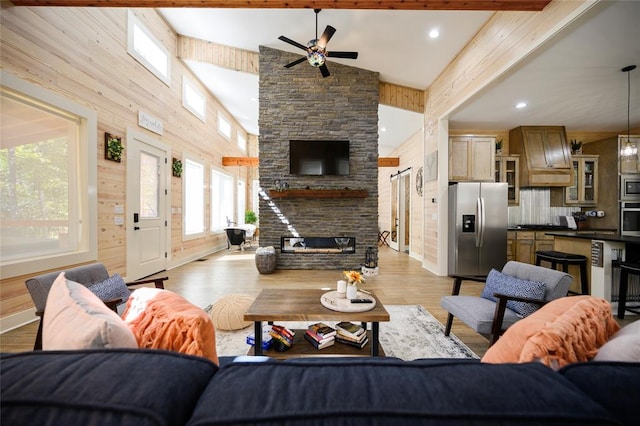 living room featuring beamed ceiling, light wood-type flooring, a stone fireplace, and a wealth of natural light