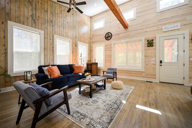 living room with ceiling fan, beam ceiling, high vaulted ceiling, hardwood / wood-style floors, and wood walls