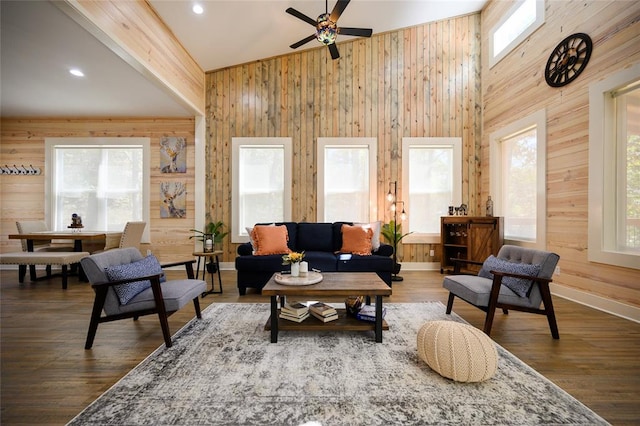 living room with a high ceiling, hardwood / wood-style flooring, ceiling fan, and wooden walls