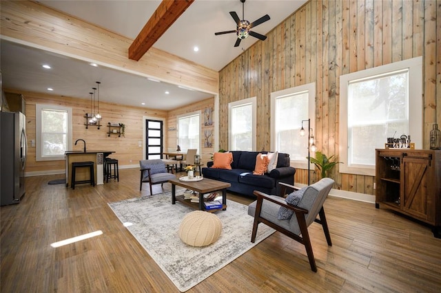 living room with wood walls, high vaulted ceiling, hardwood / wood-style flooring, ceiling fan, and beamed ceiling