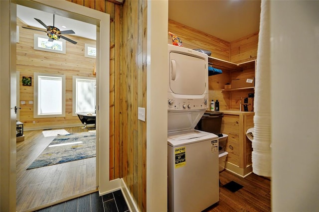 laundry area featuring wood walls, dark hardwood / wood-style flooring, ceiling fan, and stacked washer and clothes dryer