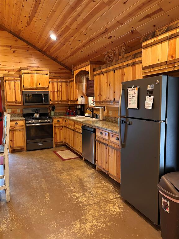 kitchen with lofted ceiling, sink, wooden walls, appliances with stainless steel finishes, and wood ceiling