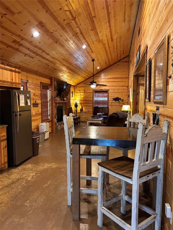 dining area with wood ceiling, ceiling fan, a fireplace, concrete floors, and lofted ceiling