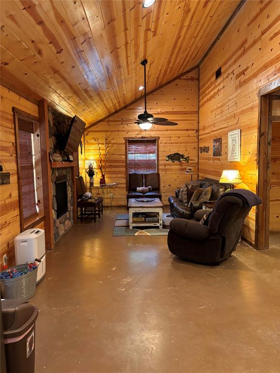 living room featuring wooden ceiling, a stone fireplace, wooden walls, vaulted ceiling, and concrete flooring