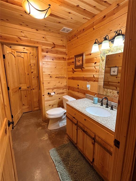 bathroom with wood walls, concrete flooring, toilet, vanity, and wood ceiling