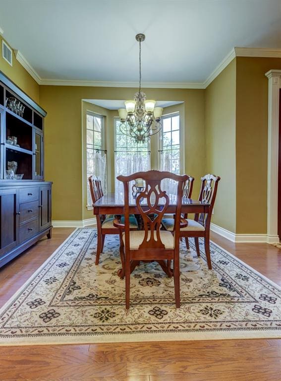 dining area with a notable chandelier, plenty of natural light, crown molding, and hardwood / wood-style floors